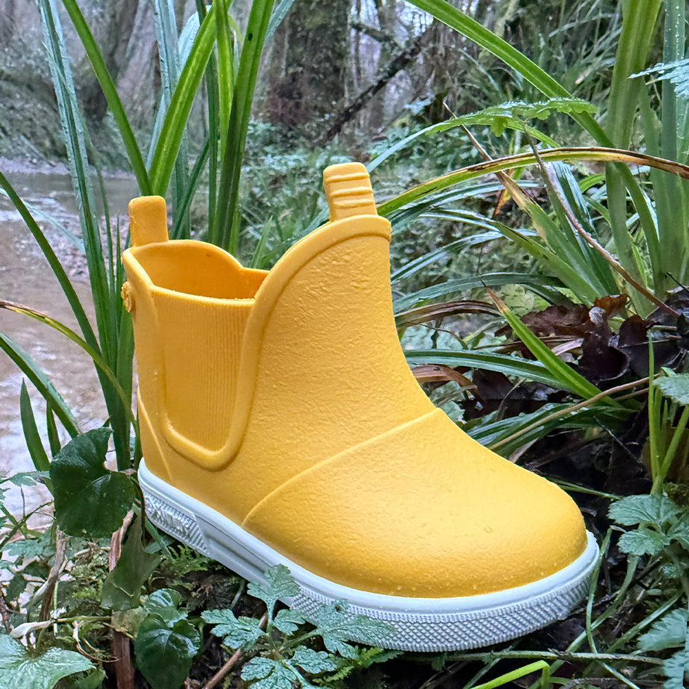 Image of a pair of Boatilus Baby Beatly boots in yellow and white on a patch of grass