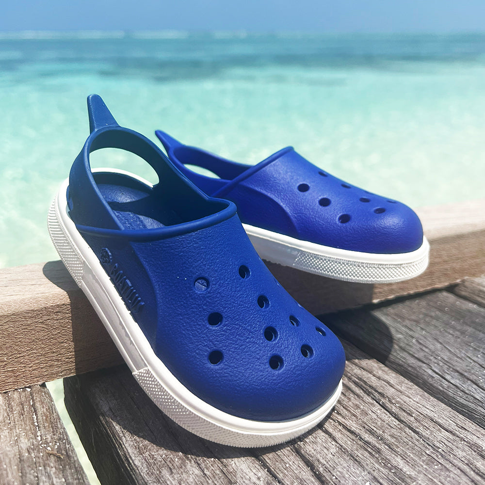 Image of a pair of Boatilus Cloggy sandals in blue on a deck near the sea