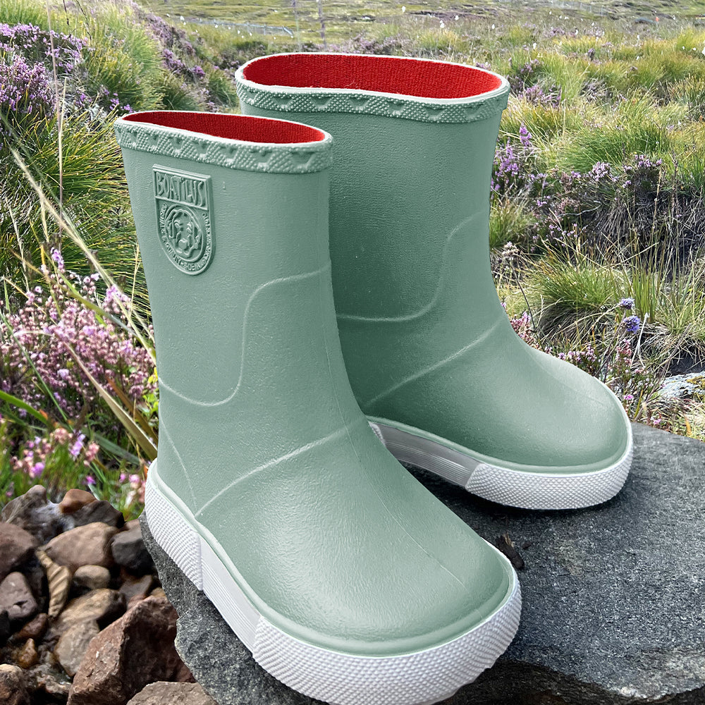 Image of a pair of Boatilus Nautic boots in green and white on a rock on a grassy field